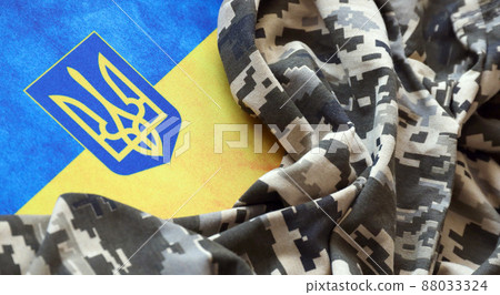 Ukrainian flag and coat of arms with fabric with texture of pixeled camouflage. Cloth with camo pattern in grey, brown and green pixel shapes with Ukrainian trident sign Ukrainian flag and coat of arms with fabric with texture of pixeled camouflage. Cloth with camo pattern in grey, brown and green pixel shapes with Ukrainian trident sign 88033324