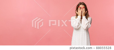 Portrait of silly cute girl with blond short hair, wear white dress, hiding face behind hands, promise to wait for signal but peeking through fingers, cant resist temptation, stand pink background 88033328