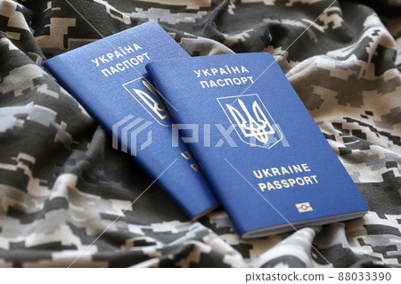 Ukrainian foreign passport on fabric with texture of military pixeled camouflage. Cloth with camo pattern in grey, brown and green pixel shapes and Ukrainian ID 88033390