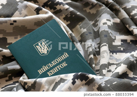 Ukrainian military ID on fabric with texture of pixeled camouflage. Cloth with camo pattern in grey, brown and green pixel shapes with Ukrainian army personal token 88033394