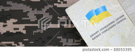 Ukrainian foreign passport on fabric with texture of military pixeled camouflage. Cloth with camo pattern in grey, brown and green pixel shapes and Ukrainian ID 88033395