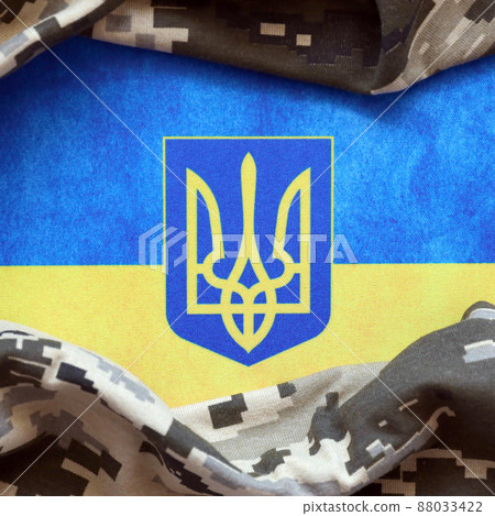 Ukrainian flag and coat of arms with fabric with texture of pixeled camouflage. Cloth with camo pattern in grey, brown and green pixel shapes with Ukrainian trident sign Ukrainian flag and coat of arms with fabric with texture of pixeled camouflage. Cloth with camo pattern in grey, brown and green pixel shapes with Ukrainian trident sign 88033422
