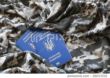 Ukrainian foreign passport on fabric with texture of military pixeled camouflage. Cloth with camo pattern in grey, brown and green pixel shapes and Ukrainian ID Ukrainian foreign passport on fabric with texture of military pixeled camouflage. Cloth with camo pattern in grey, brown and green pixel shapes and Ukrainian ID 88033502
