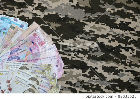 Ukrainian hryvnya bills on fabric with texture of Ukrainian military pixeled camouflage. Cloth with camo pattern in grey, brown and green pixel shapes 88033523