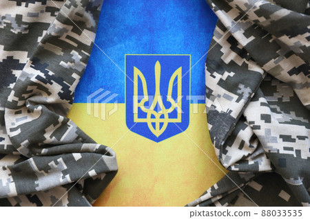 Ukrainian flag and coat of arms with fabric with texture of pixeled camouflage. Cloth with camo pattern in grey, brown and green pixel shapes with Ukrainian trident sign Ukrainian flag and coat of arms with fabric with texture of pixeled camouflage. Cloth with camo pattern in grey, brown and green pixel shapes with Ukrainian trident sign 88033535