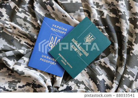 Ukrainian military ID and foreign passport on fabric with texture of pixeled camouflage. Cloth with camo pattern in grey, brown and green shapes with Ukrainian army personal token and passport. 88033541