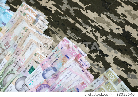 Ukrainian hryvnya bills on fabric with texture of Ukrainian military pixeled camouflage. Cloth with camo pattern in grey, brown and green pixel shapes 88033546