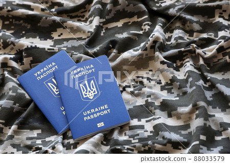 Ukrainian foreign passport on fabric with texture of military pixeled camouflage. Cloth with camo pattern in grey, brown and green pixel shapes and Ukrainian ID 88033579