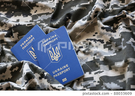 Ukrainian foreign passport on fabric with texture of military pixeled camouflage. Cloth with camo pattern in grey, brown and green pixel shapes and Ukrainian ID 88033609
