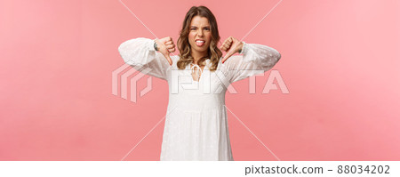 Portrait of picky and moody cute blond girl complaining on bad service, awful quality, show thumbs-down and tongue with dislike grimacing, telling about disgusting experience, pink background Portrait of picky and moody cute blond girl complaining on bad service, awful quality, show thumbs-down and tongue with dislike grimacing, telling about disgusting experience, pink background 88034202