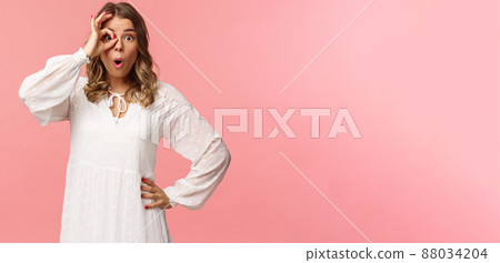 Portrait of amazed and intrigued young blond girl seeing something awesome, look from okay sign with startled excited expression, fold lips say wow, pop eyes at camera, pink background 88034204