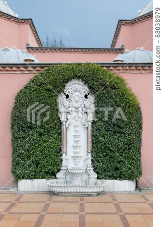 White marble sculpted wall fountain surrounded by green leaves over pink stone wall and tiled orange ceramic floor in Sultan Ahmed square, Istanbul, Turkey White marble sculpted wall fountain surrounded by green leaves over pink stone wall and tiled orange ceramic floor in Sultan Ahmed square, Istanbul, Turkey 88038979