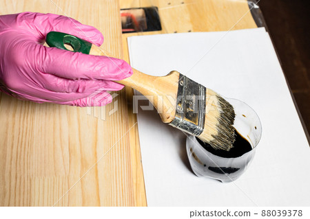 gloved hand dips brush into jar of wood stain 88039378