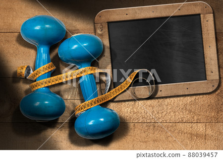 Old Blue Dumbbells with Tape Measure and Empty Blackboard 88039457