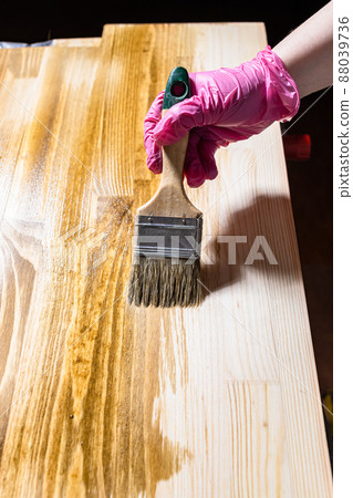 solid board is hued with wood stain by paintbrush 88039736