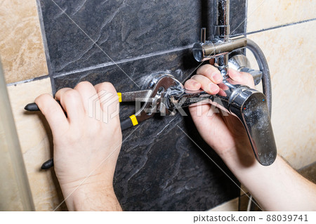 plumber unscrews shower faucet on tiled wall plumber unscrews shower faucet on tiled wall 88039741