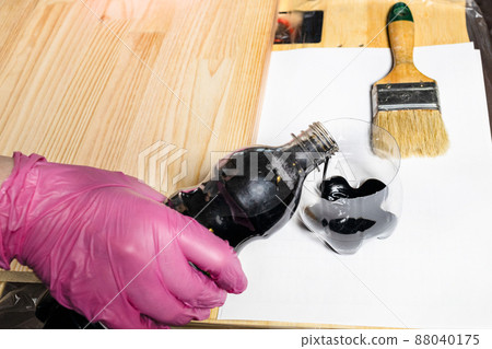 gloved hand pours wood stain from bottle into jar 88040175