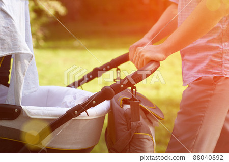 A young dad walking in the park with a baby in a stroller. Close-up of men's hands with a stroller. Father's Day concept. High quality photo 88040892