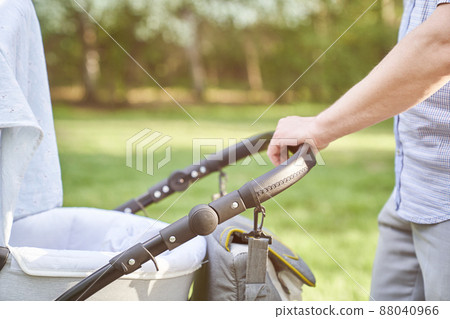 A young dad walking in the park with a baby in a stroller. Close-up of men's hands with a stroller. Father's Day concept. High quality photo 88040966