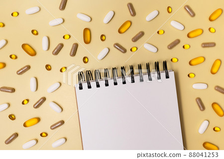 Pills lie around a notepad and pen. 88041253