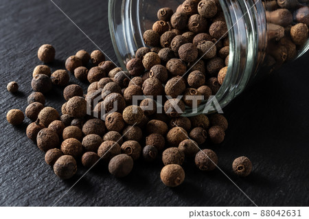 Allspice jamaica pepper grains spilled out of the glass jar over black slate background. 88042631