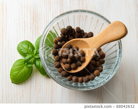 Wooden spoon with allspice jamaica pepper in a glass bowl and fresh basil leaves. 88042632