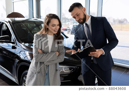 an employee of a car shop draws up documents for a new car for a woman buyer an employee of a car shop draws up documents for a new car for a woman buyer 88043608
