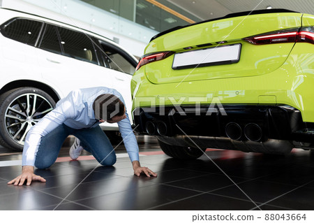 a man examines in detail the exhaust system of a new car in a car dealership 88043664