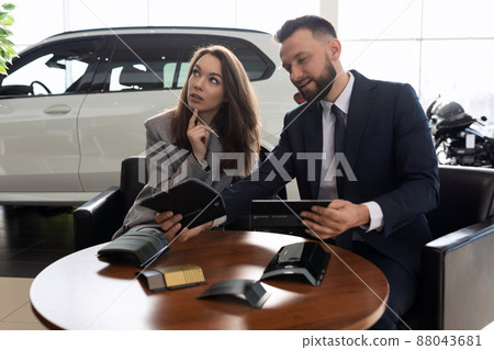 a young married couple in a car dealership chooses a car sits with a smile in the trunk of a a young married couple in a car dealership chooses a car sits with a smile in the trunk of a 88043681