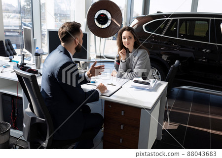 a young woman draws up a deal to buy a new car and insure it at a car dealership a young woman draws up a deal to buy a new car and insure it at a car dealership 88043683