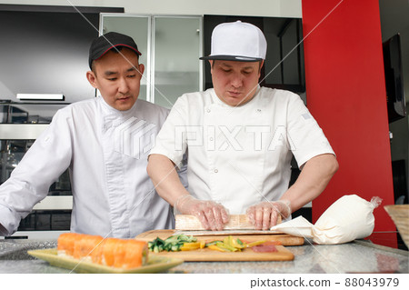 Two happy young asian chefs dressed in white uniform preparing traditional japanese sushi set in interior of modern professional kitchen. 88043979