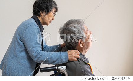 An old married woman who puts her hand on the shoulder of an elderly husband in a wheelchair An old married woman who puts her hand on the shoulder of an elderly husband in a wheelchair 88044209