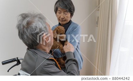 An elderly man in a wheelchair reaching for his dog held by an elderly woman 88044242