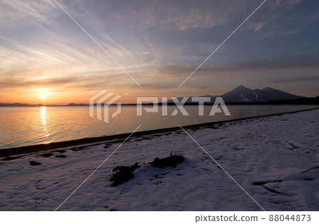 Evening view of Lake Inawashiro where the snow of spring remains. The collaboration between the snowy lakeside, the orange sunset and Mt. Bandai is beautiful. 88044873