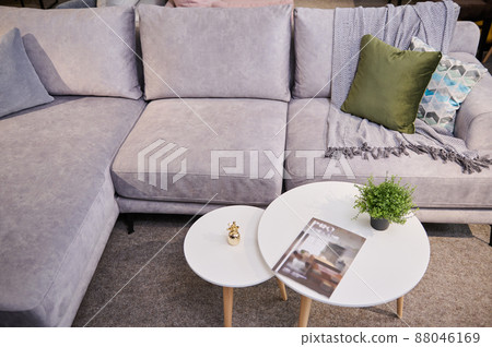 Top view of a stylish comfortable sofa upholstered with light velour fabric with colorful pillows and a small journal table on display in the furniture store showroom 88046169