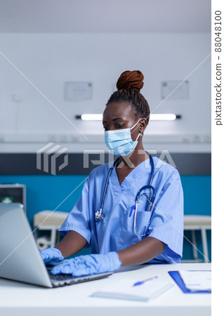 Clinic medical nurse looking for patient disease records and clinical documents while wearing virus protection mask. Hospital staff worker using laptop to search treatment medicine and patient Clinic medical nurse looking for patient disease records and clinical documents while wearing virus protection mask. Hospital staff worker using laptop to search treatment medicine and patient 88048100