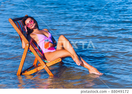 Full length of pretty girl in pink bathing suit relaxing on the beach while lying at the deck chair 88049172