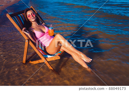 Beautiful sexy girl in a pink bathing suit suntanning on the beach while lying at the deck chair 88049173