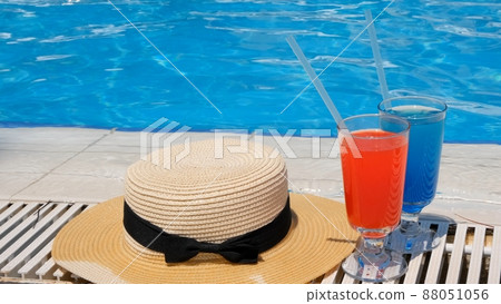Two colorful cocktail glasses pink and blue, sun hat on the edge of the swimming pool, close up 88051056