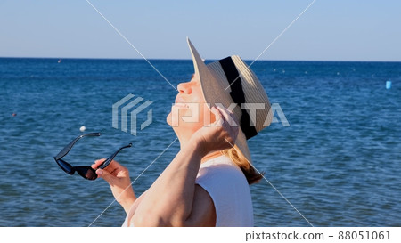 happy 50 year old woman in straw hat and sunglasses enjoying the sun against the blue sea background 88051061