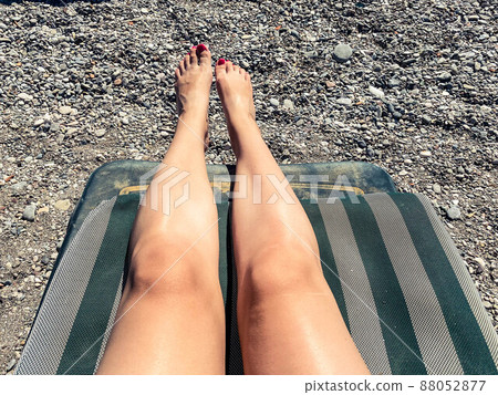 The legs of a beautiful curvy blonde with long hair in a blue swimsuit gets a tan while lying in a sun lounger on a beach with a blue sea. 88052877