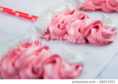 Meringue in the form of pink Christmas hats, with a white bumbone and rim lies on white parchment. High quality photo Meringue in the form of pink Christmas hats, with a white bumbone and rim lies on white parchment. High quality photo 88053991