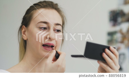 The girl paints her lips with lipstick. Close-up of the face. Macro photography of A Woman Wearing lipstick. The face macro. The girl looks in a small mirror The girl paints her lips with lipstick. Close-up of the face. Macro photography of A Woman Wearing lipstick. The face macro. The girl looks in a small mirror 88056819