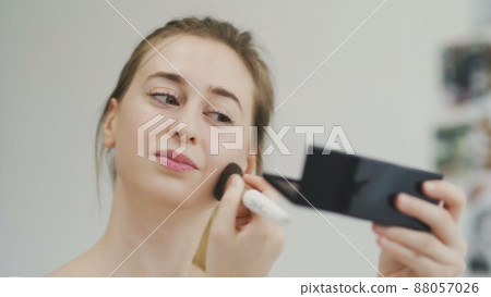 A young woman does her makeup while looking in a small mirror A young woman does her makeup while looking in a small mirror 88057026