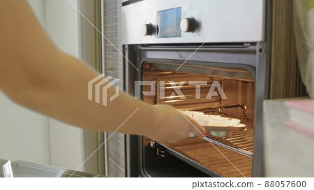 Close-up view of young woman open the oven and puts on the baking dish with dough. Female cooking the cupcakes. Close-up view of young woman open the oven and puts on the baking dish with dough. Female cooking the cupcakes. 88057600