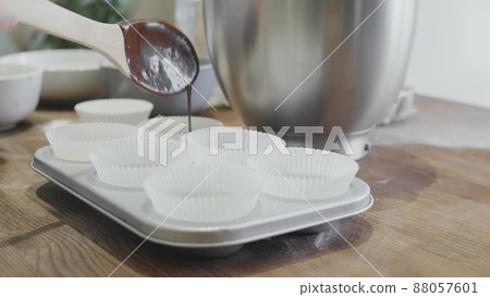 The cook pours chocolate into cupcake molds on the kitchen table The cook pours chocolate into cupcake molds on the kitchen table 88057601