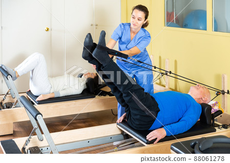 Rehabilitation physician controlling senior man exercising on pilates reformer 88061278
