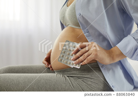 Future mother takes vitamin and mineral pills to ensure she gets enough nutrients for her baby in her womb. Pregnant woman with bare belly holding blister packs, close up. Pregnancy and health concept 88063840