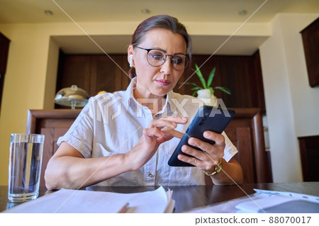 Face of a mature woman looking at a webcam, talking, at her desk at home. Face of a mature woman looking at a webcam, talking, at her desk at home. 88070017