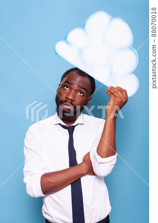 Portratit of accountant in white shirt looking up at white paper idea cloud brainstorming standing in front of blue background. African american entrepreneur thinking under thought bubble. Portratit of accountant in white shirt looking up at white paper idea cloud brainstorming standing in front of blue background. African american entrepreneur thinking under thought bubble. 88070018